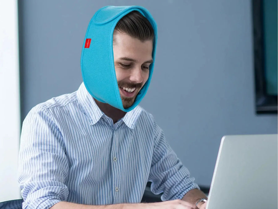 A man wearing a blue ice wrap around his head and chin while using a laptop.