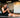A man sitting on a gym mat using an electrical muscle stimulation device on his arm and legs.