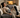 A woman relaxing on a grey sofa with a heating pad on her stomach and a blanket.
