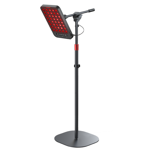 Woman lying down receiving red light therapy from an adjustable floor lamp device.