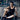 Smiling man in gym using TENS unit electrode pads on his arm and leg while looking at smartphone.