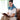 Woman wearing a blue weighted heating pad for neck and shoulders while reading.