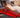 Woman lying on a red light therapy mat while using a smartphone on a bed.