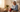 Elderly woman using a red light therapy device on her knee while sitting on a sofa.