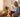Elderly woman using a red light therapy device on her knee while sitting on a sofa.