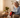 Elderly woman using a red light therapy device on her knee while sitting on a sofa.