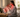 A woman in pajamas sits on a bed facing a glowing red light therapy panel on a nightstand.