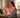 A woman in pajamas sits on a bed facing a glowing red light therapy panel on a nightstand.