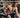 A man sitting in a gym with many TENS unit electrode pads placed over his torso and arms.