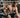 A man sitting in a gym with many TENS unit electrode pads placed over his torso and arms.