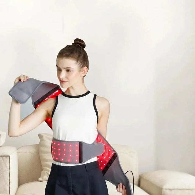 Woman wearing a red light therapy belt wrap around her waist and shoulder.