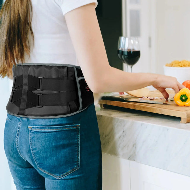 A woman in a kitchen wearing a black electric heated back support belt while preparing food.